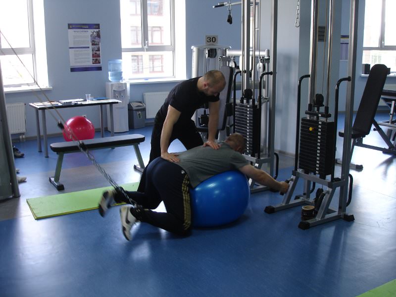 Тренер работает с пациентом на гимнастическом мяче.